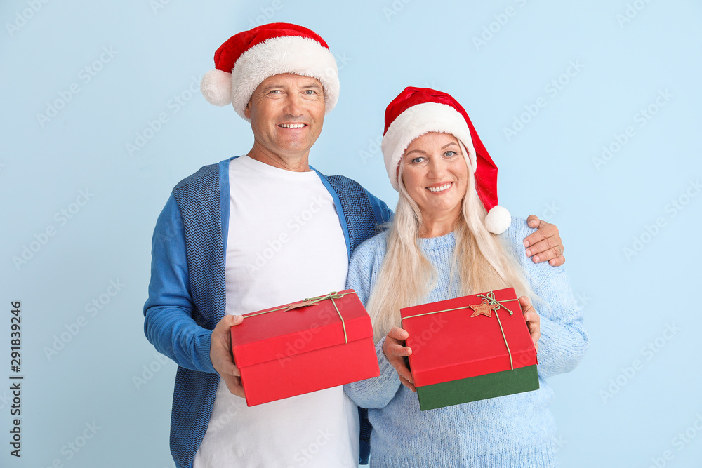 Happy mature couple with Christmas gifts on light background