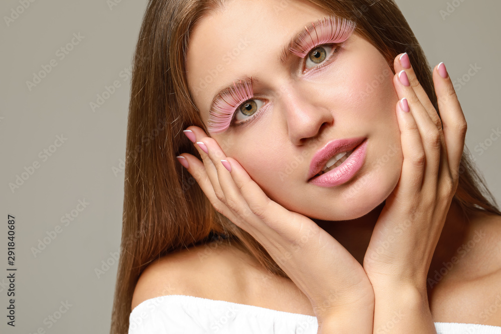 Young woman with creative eyelashes on grey background