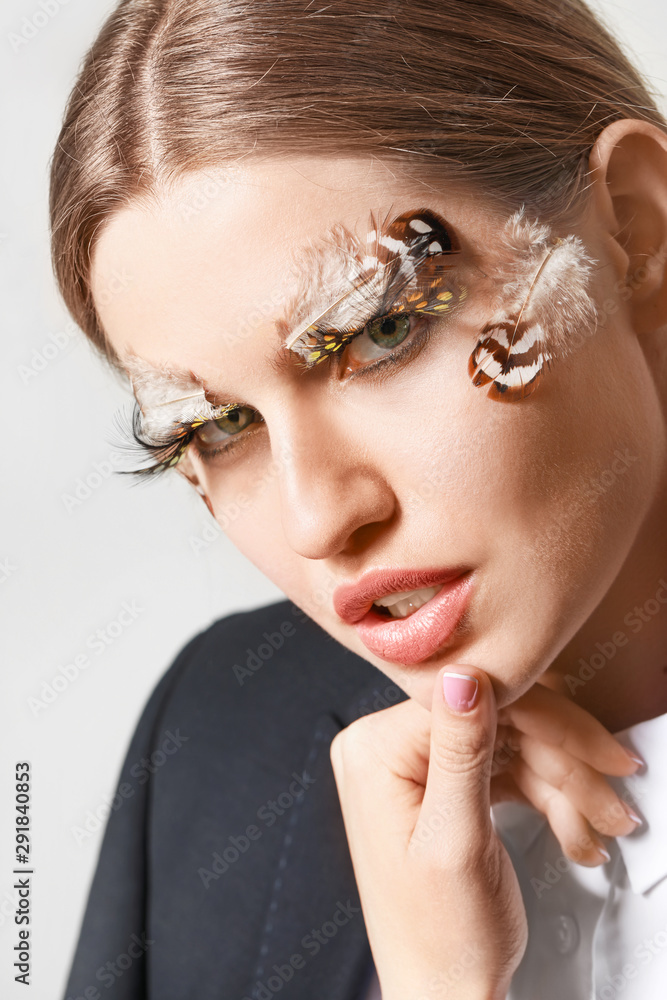Young woman with creative eyelashes and eyebrows on grey background