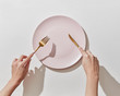 © Yaroslav Danylchenko/Stocksy - Fork and knife in women's hands with empty plate on a white background, copy space. Waiting for dinner. Flat lay