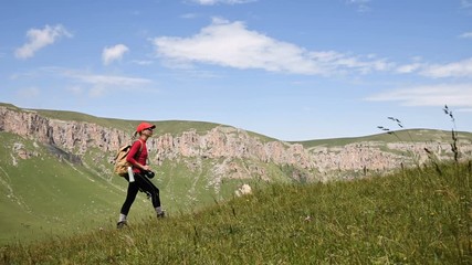 Wall Mural - Girl photographer goes up the hill uphill against the backdrop of cliffs of a plateau and the sky with clouds. Concept photo tours for landscape photographers