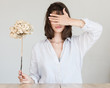 © papa - The young woman covers her eyes with one hand while holding a dried hydrangea flower in the other.