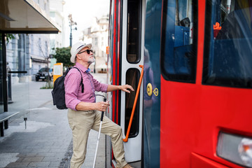 Wall Mural - Senior blind man with white cane getting on public transport in city.