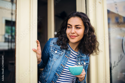 Cuadros en Lienzo A beautiful young woman with tablet and coffee standing at the front door in cafe