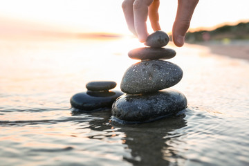 Woman stacking dark stones on sand near sea, space for text. Zen concept