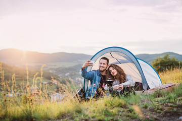 Wall Mural - young tourist couple travellers with tent shelter sitting in nature, taking selfie.