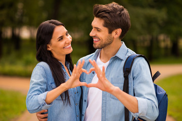 Poster - Photo of cute pair standing together in green summer park making heart figure with arms wear denim outfit