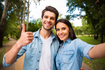 Poster - Portrait of lovely guy and girl with brunet haircut making photo showing thumb up sign wearing denim jeans shirt outdoors