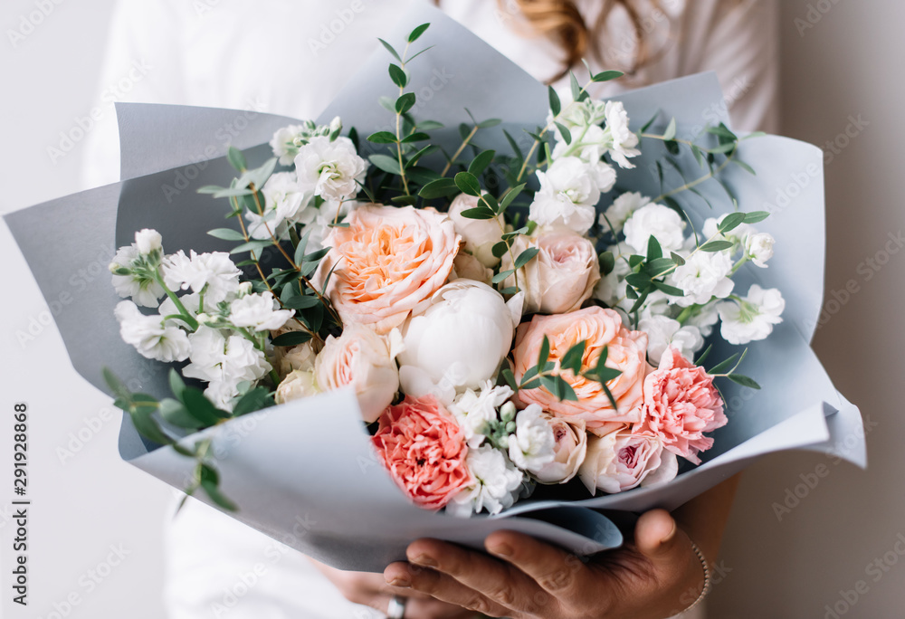 Very nice young woman holding a beautiful blossoming flower bouquet of fresh mattiolas, roses, peony, carnations, eucalyptus in pastel pink colour on the grey wall background 