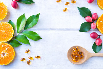 Vitamin supplements on wooden spoon with healthy fruit orange and Koronda Fruit (wild berries) with green leaf on white wooden background.Top view.