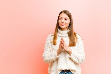 young pretty woman feeling proud, mischievous and arrogant while scheming an evil plan or thinking of a trick against pink background