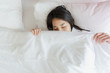 © anon - Woman stretching in bed after waking up, back view. Woman sitting near the big white window while stretching on bed after waking up with sunrise at morning, back view.
