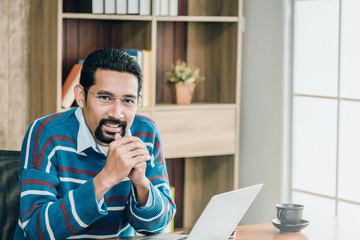 Arab businessman in casual clothes wearing glasses working in the office with laptop and a cup of coffee on working table.