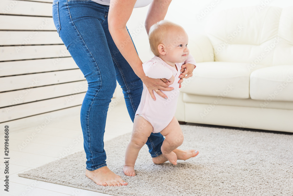 Baby taking first steps with mother's help at home - obrazy, fototapety, plakaty 