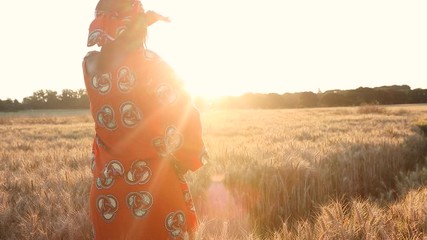 Wall Mural - HD Video clip of African woman farmer in traditional clothes standing in a field of crops, wheat or barley, in Africa at sunset or sunrise