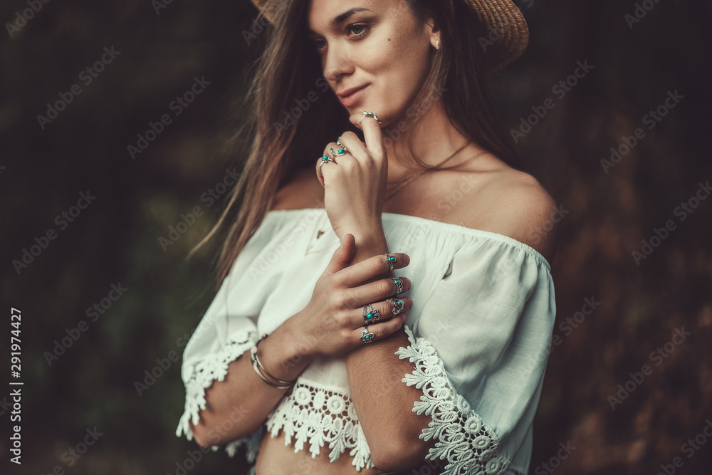 Obraz na płótnie Beautiful fashionable boho chic woman in straw hat and in a white short blouse with silver turquoise jewelry. Boho fashion. Stylish girl with silver rings using hippie style. w salonie