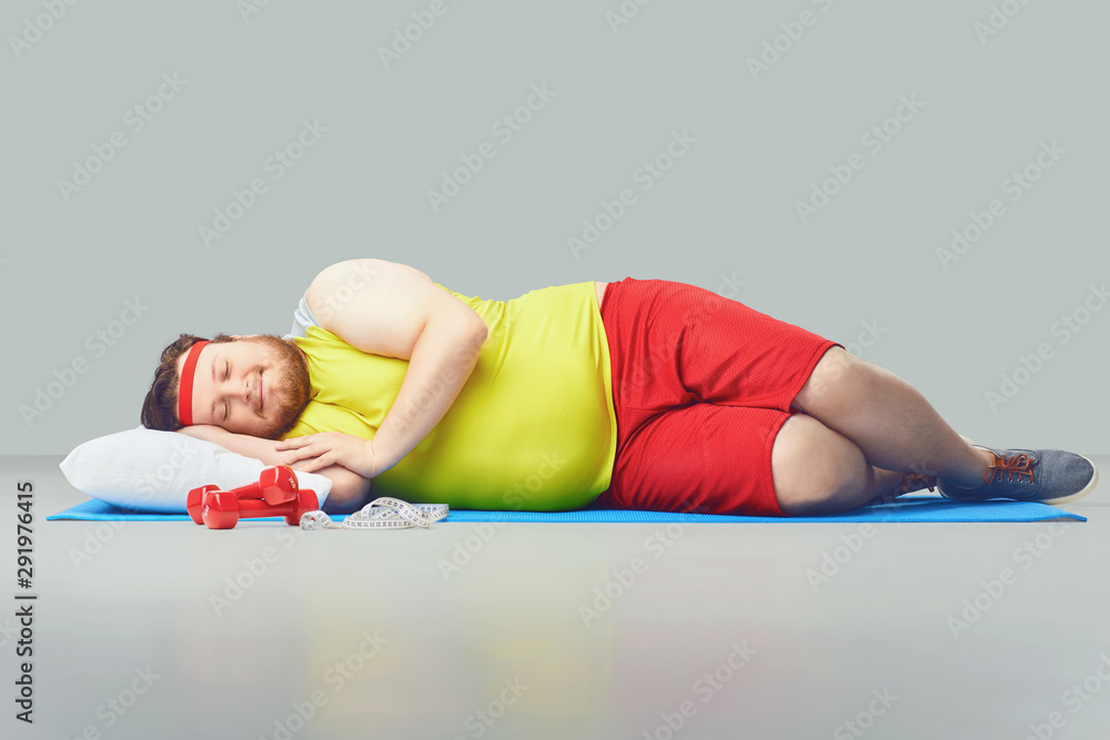Lazy fat funny man is sleeping on a gray background. - obrazy, fototapety, plakaty 