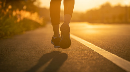 Wall Mural - Runner feet running on road closeup on shoe. Woman fitness sunrise jog workout wellness concept. Young fitness woman runner athlete running at road