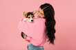 © LIGHTFIELD STUDIOS - smiling woman holding cute Corgi puppy, isolated on pink