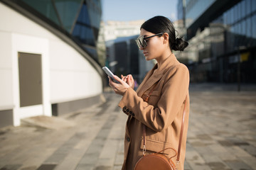 business woman in a suit and sunglasses. In her hands is a mobile phone. Building in the background