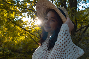 Woman in romantic attire and straw hat relaxing outdoor in autumn or summer park and enjoying weather and sunset.