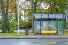 Empty Glass Bus Stop With Yellow Bench Near Road In City