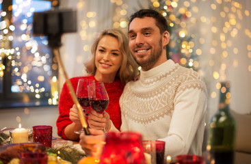 Canvas Print - christmas, holidays, technology and people concept - happy couple in taking picture by selfie stick at home dinner