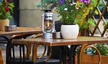 Wooden Table And Chairs For Eating Near An Outdoor Restaurant, A Candle In A Glass Candlestick And A Flower In A Pot