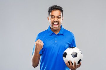 sport, leisure games and success concept - happy indian man or football fan with soccer ball celebrating victory over grey background