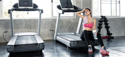 Wall Mural - Asian women hold flask, sit and rest tired on the treadmill.