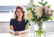 © papa - Portrait of a young beautiful woman sitting at a table with a bouquet of flowers in a vase in a bright room.