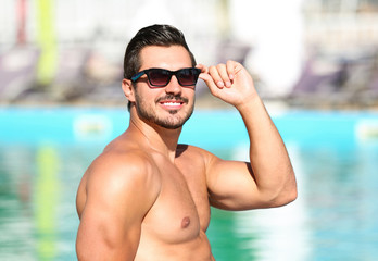 Wall Mural - Handsome young man with sunglasses near swimming pool on sunny day