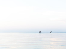 Two Boats Anchored Off Shore With An Outgoing Tide And Clear Sky At Sunset.