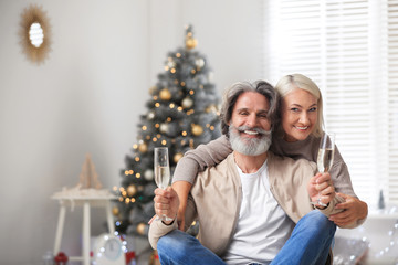 Wall Mural - Happy mature couple with glasses of champagne celebrating Christmas at home