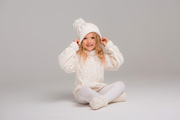 Winter clothes. Portrait of a little curly-haired girl in a knitted white winter hat. little blonde girl in white knitted hat and sweater smiling light background isolate, space for text