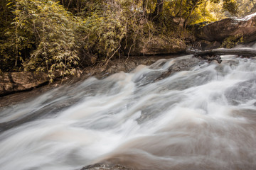 Natural blurred background of waterfalls, fast-flowing currents and water droplets from the wind blowing among the rocks and surrounded by big trees, spontaneous beauty