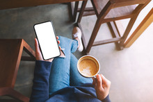 Top View Mockup Image Of A Woman Holding White Mobile Phone With Blank Screen While Drinking Coffee
