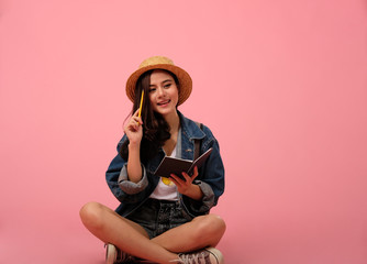 portrait of smiling asian woman wearing jeans jacket with notebook & pencil. studio shot