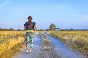 Wall Mural - Back view of woman running and exercising on the path through the rice fields in the evening.