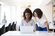 © Mangostar - Satisfied female colleagues discussing project at workplace. Business women sitting and standing at table in office, using laptop and talking. Working together concept