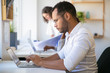 © Mangostar - Focused male employee working on project in office. Man and women in casual sitting and standing at table and using laptops. Diverse staff concept