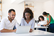 © Mangostar - Multiethnic colleagues looking at laptop screen and discussing project. Their colleagues working in background. Office workspace concept