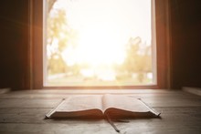 Close Shot Of Holy Bible On A Wooden Surface With The Sun Shining In The Background