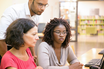 Wall Mural - adult female students consulting instructor in computer class. man and women sitting and standing at