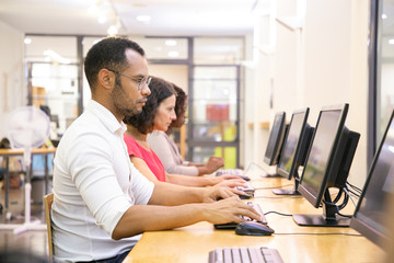 Wall Mural - diverse group of students taking online tests in computer class. line of man and women in casual sit