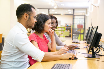 Wall Mural - diverse adult college mates working together in computer class. man and women in casual sitting at t