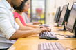 © Mangostar - Multiethnic group of students working in computer class. Row of man and women in casual sitting at table, using desktops, typing. Training center concept