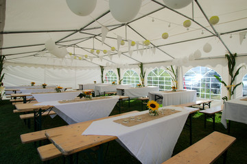 Arrangement dinner in a tent with wooden tables and benches. Decorated with sunflowers, candles and balloons.