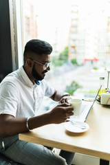 Wall Mural - Indian man using laptop computer while drinking a cup hot milk tea, outdoor cafe.