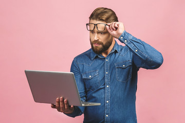 Wtf?! Omg! Oh no! Young amazed emotional brunet with bristle with sad grimace looks at screen of device, he can`t believe the bad news he received, gesturing with palms of arms.